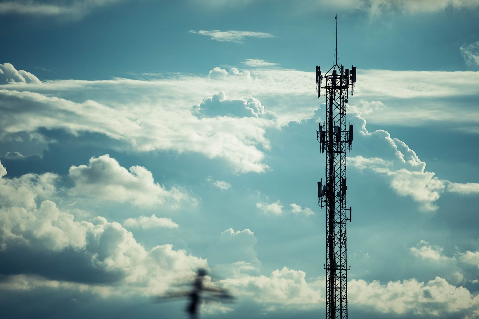 Silhouette of a mobile phone antenna standing out against a cloudy sky.