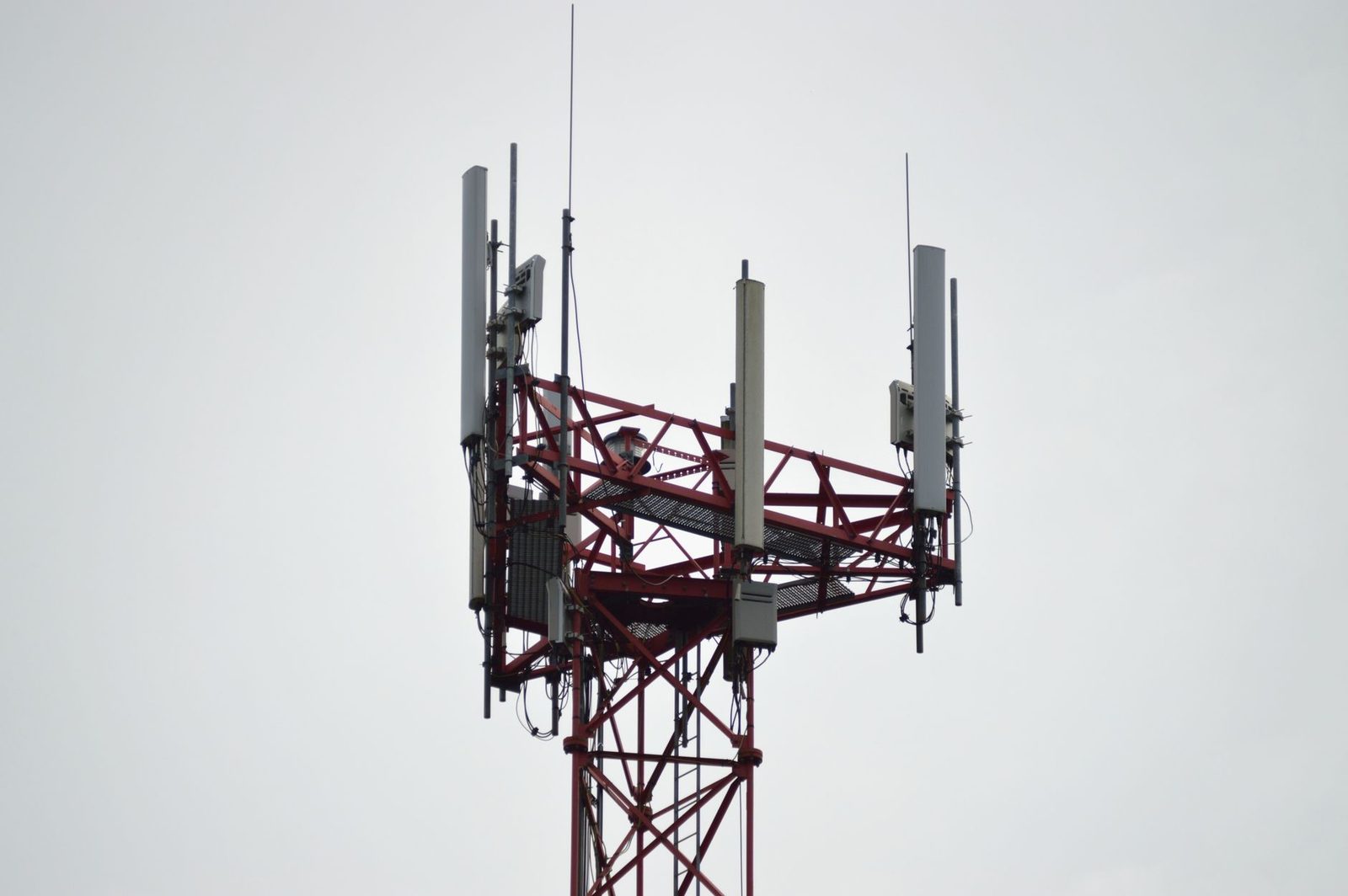 Top of a red and white telecommunications tower fitted with mobile phone relay antennas