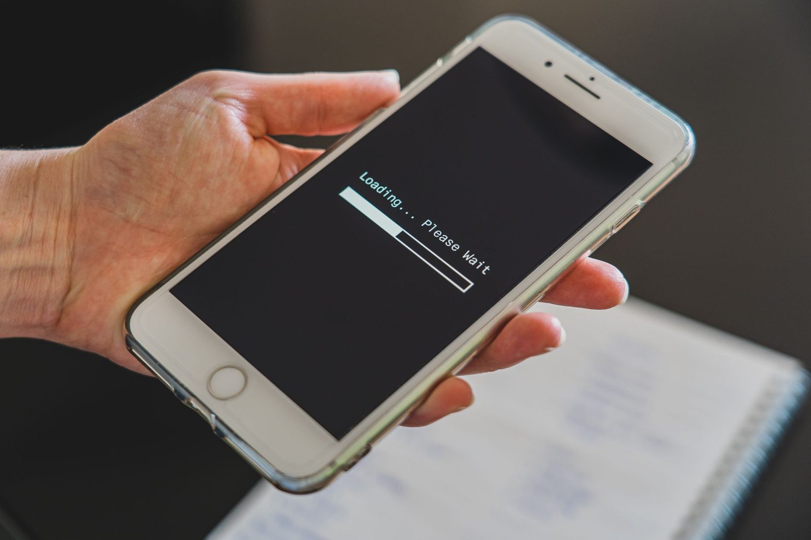 Hand holding a white smartphone displaying a loading screen, above a spiral notebook