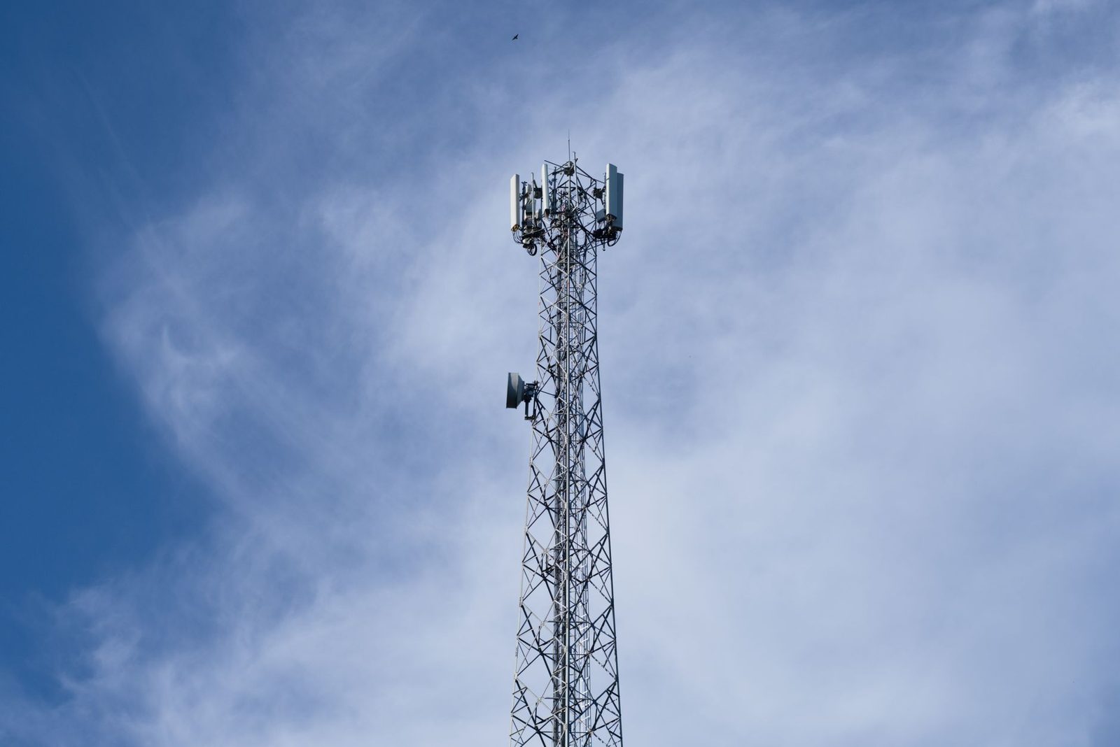 Torre de telefonía móvil con antenas repetidoras recortada contra un cielo azul con nubes