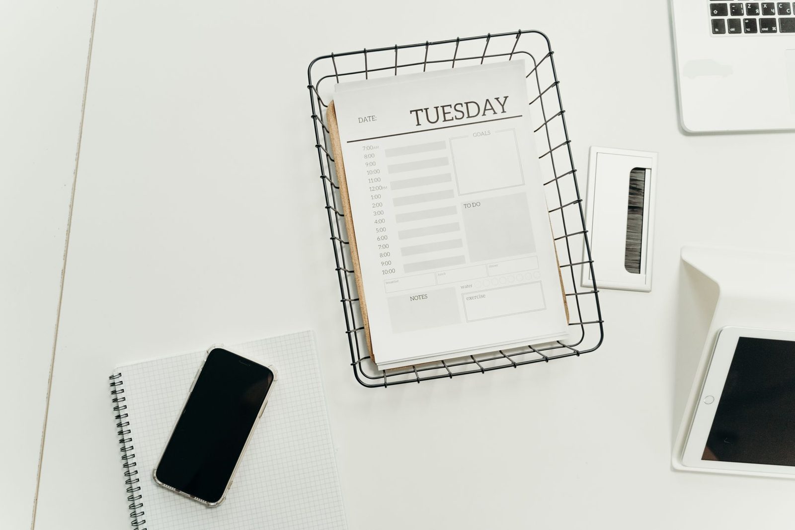 Smartphone con la pantalla en negro apoyado sobre un cuaderno, junto a una agenda de papel, un ordenador portátil y una tableta