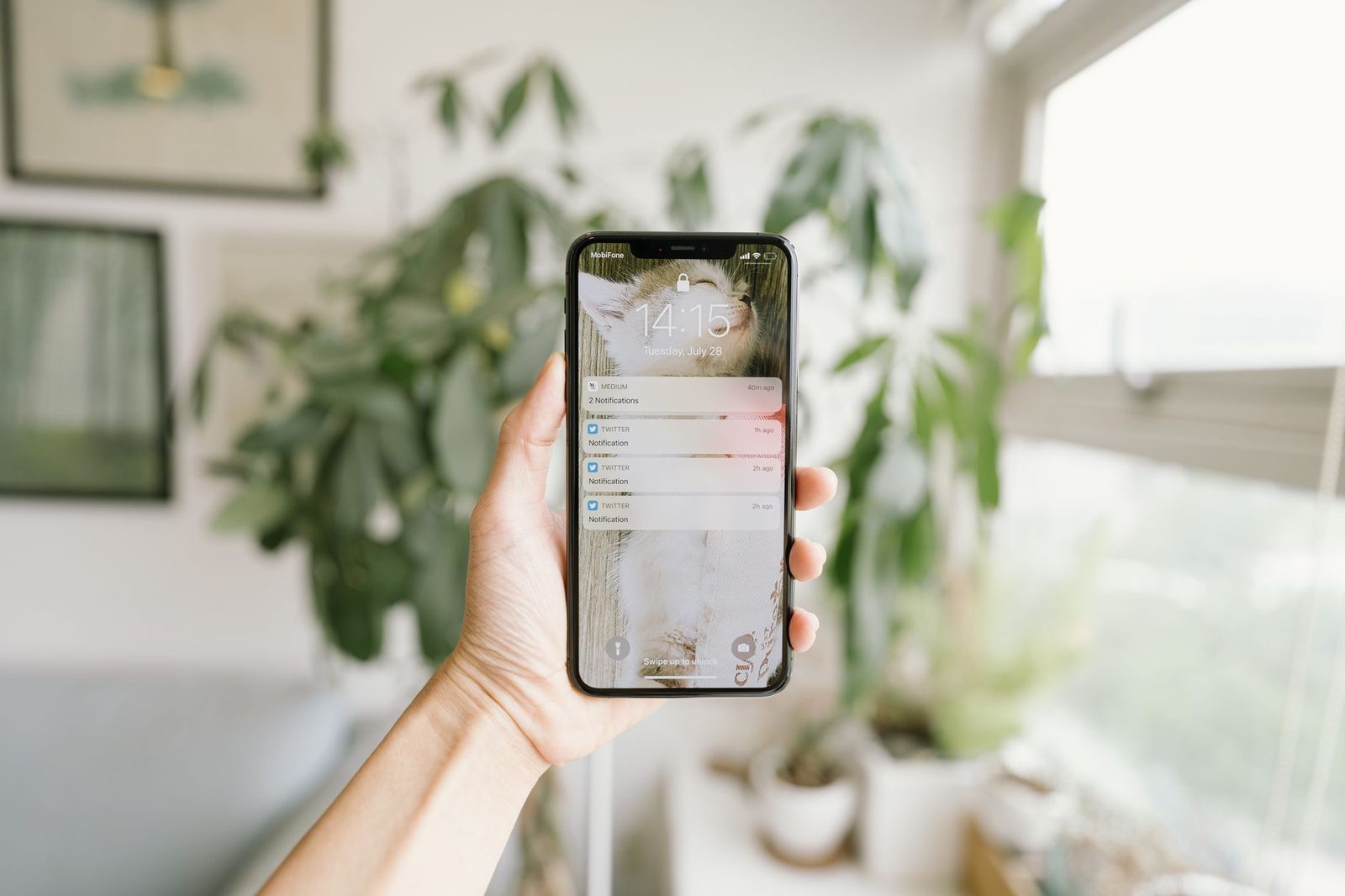 Mano sosteniendo un smartphone que muestra notificaciones en la pantalla de bloqueo, delante de unas plantas verdes