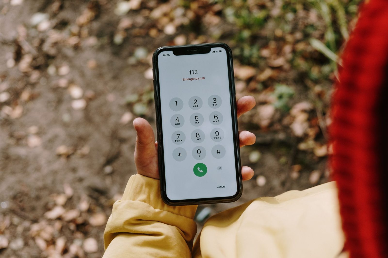 Hand met een smartphone waarop het noodoproepnummer 112 op het toetsenblok staat, buitenshuis