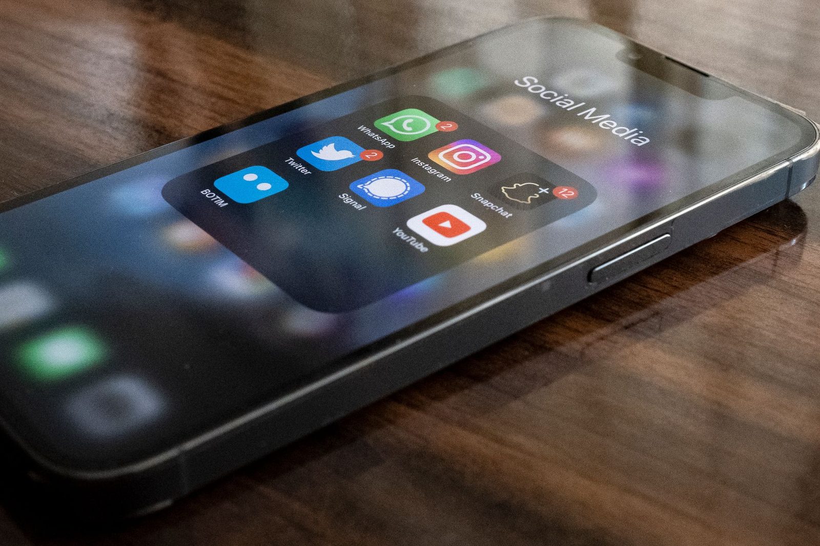 Smartphone op een houten tafel, scherm aan met een map met socialmedia-apps