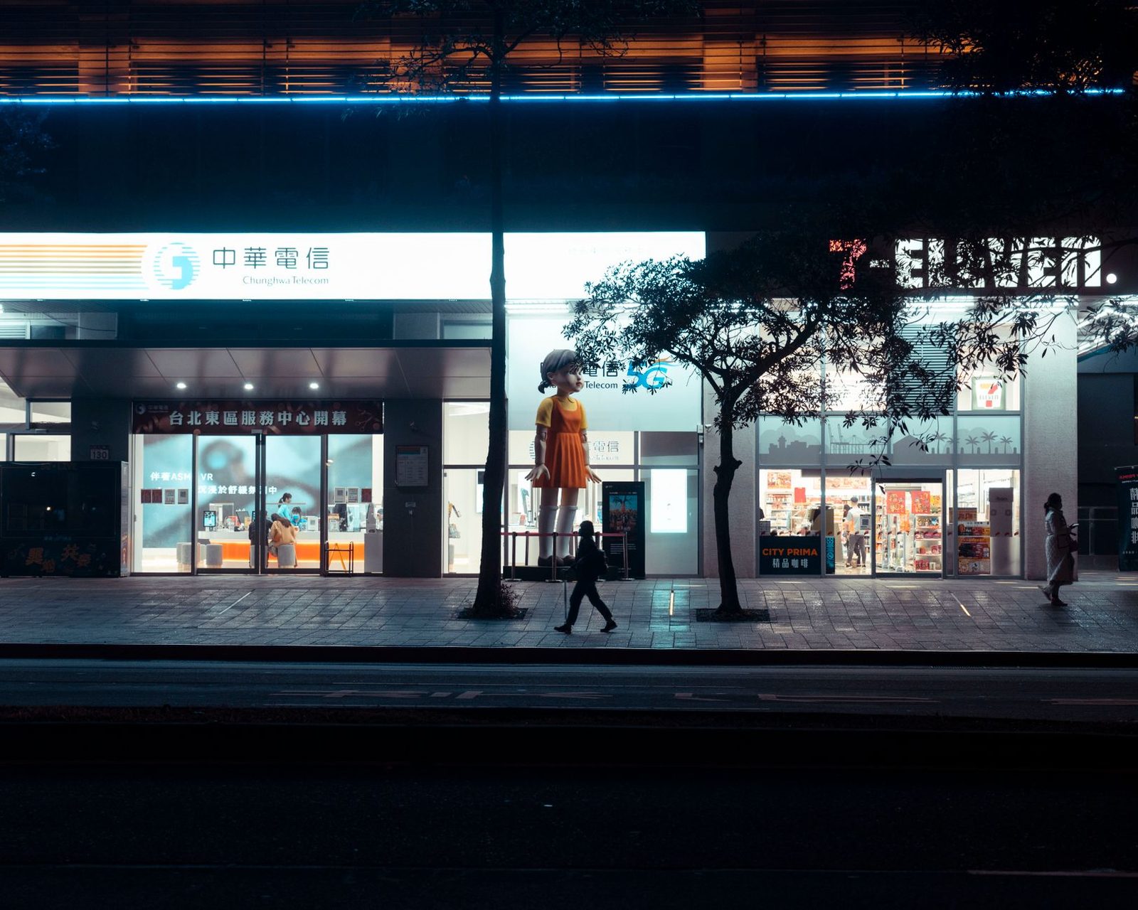 Verlichte telecomwinkel bij nacht met een 5G-uithangbord en voorbijgangers op de stoep