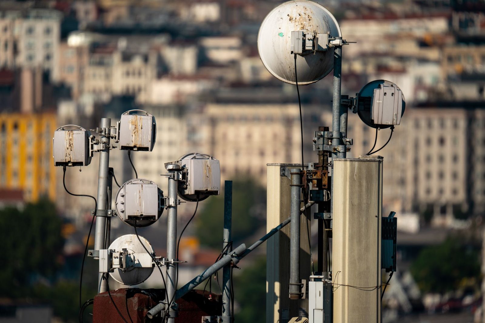 Zendmasten en satellietschotels voor mobiele telefonie op een dak, met stadsgebouwen wazig op de achtergrond