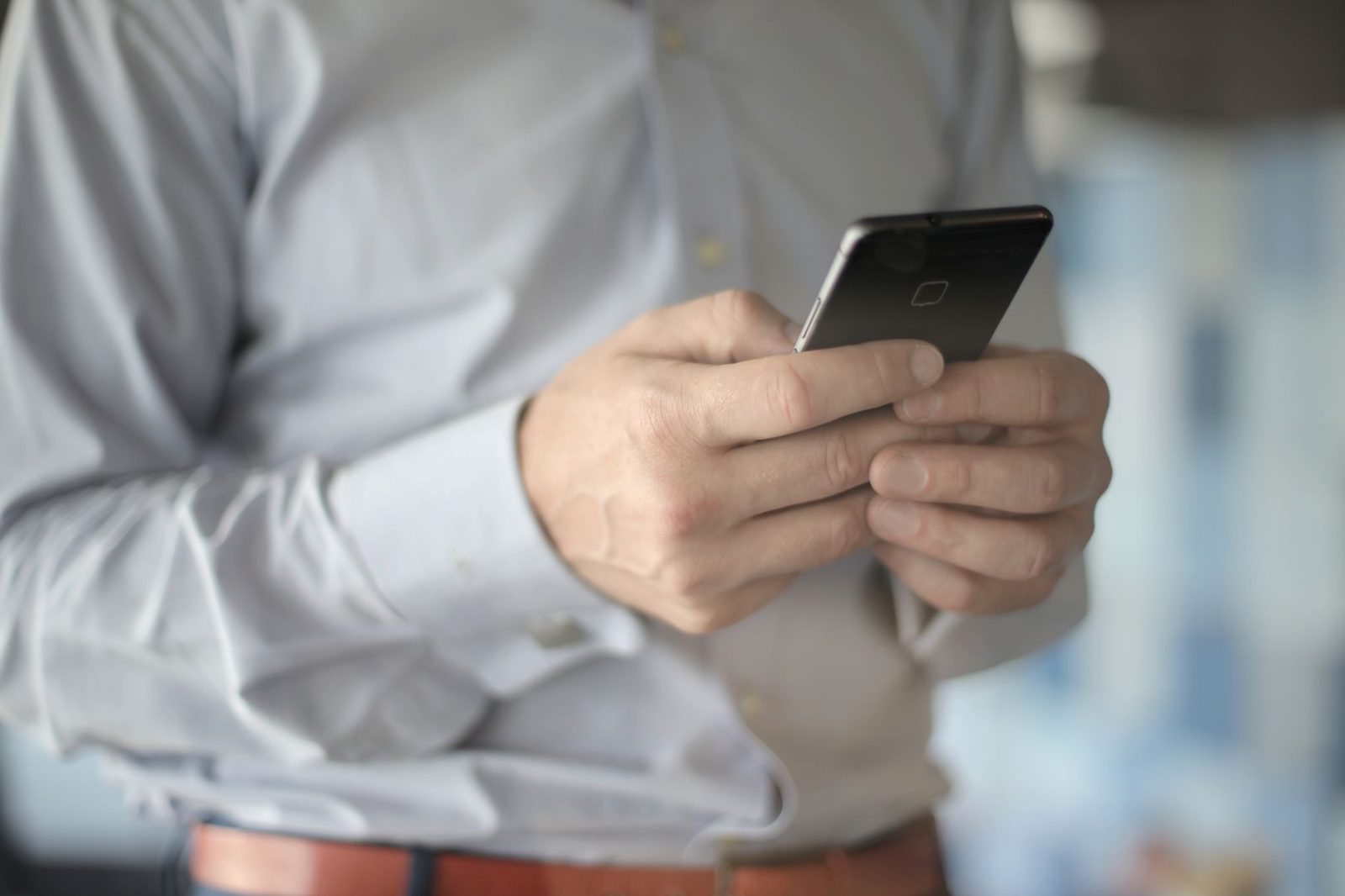 Homme en chemise claire tenant un smartphone noir dans ses mains, gros plan sur l'écran tactile