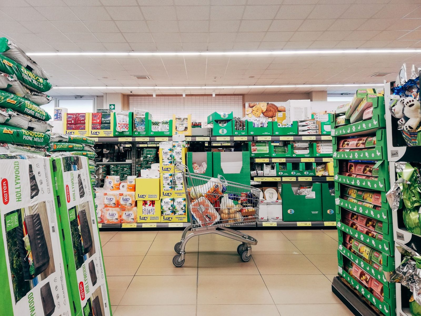 Corsie di un supermercato discount con casse verdi e un carrello pieno di prodotti nel corridoio