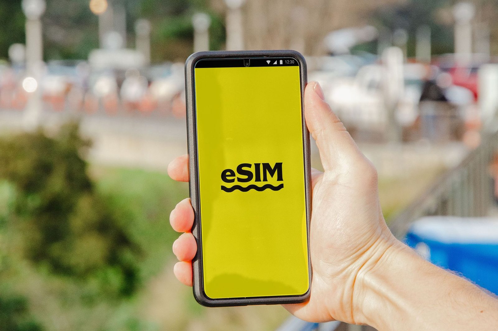 Hand die een smartphone vasthoudt met op het gele scherm het woord eSIM, buitenshuis
