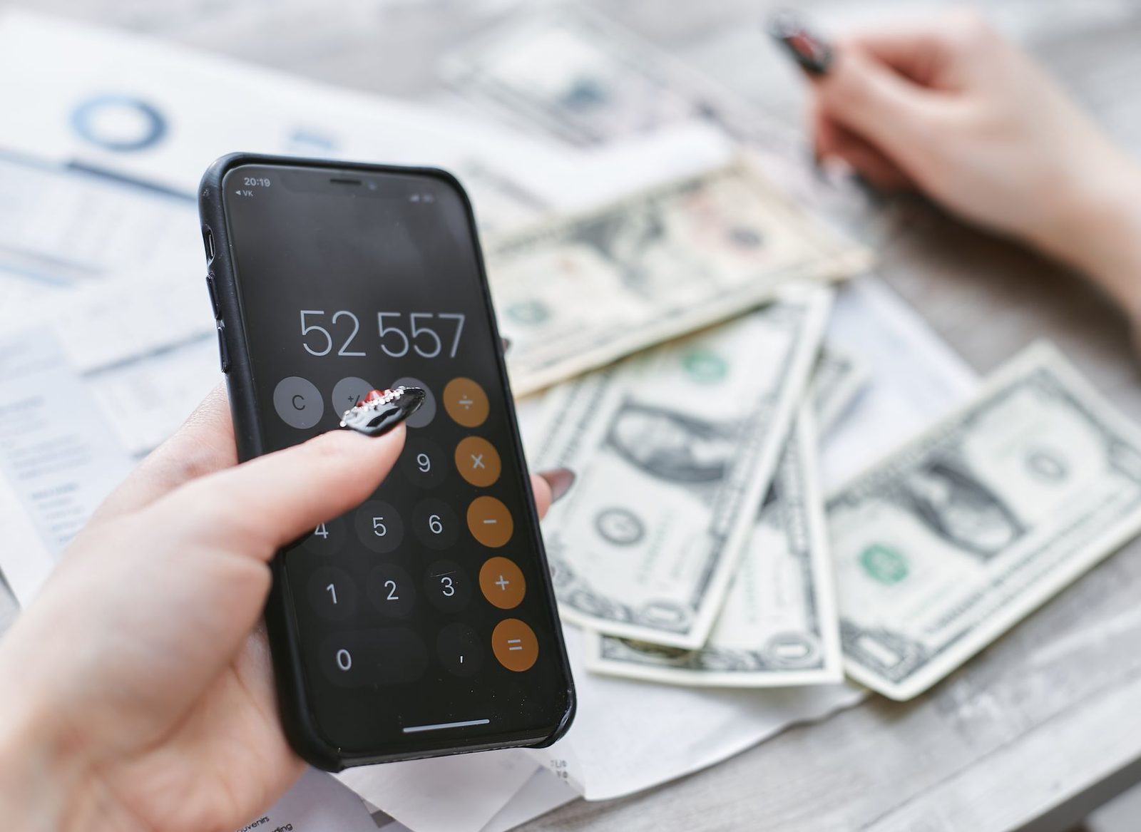 Mano che tiene uno smartphone con una calcolatrice sullo schermo sopra banconote e bollette