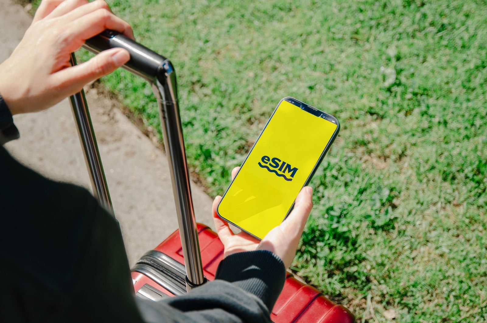 Hand hält ein Smartphone mit der Anzeige „eSIM" auf gelbem Bildschirm, daneben ein roter Koffer