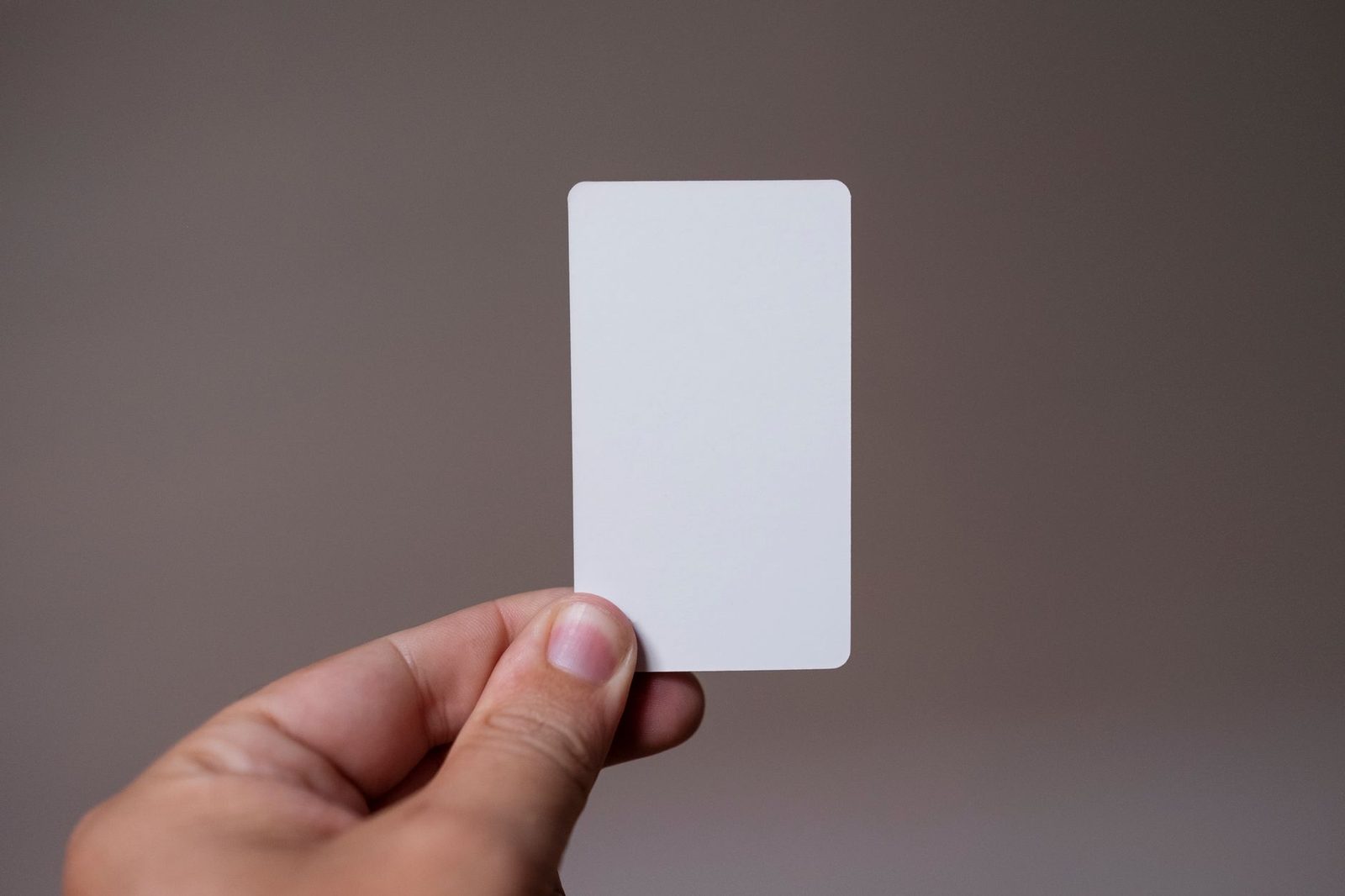 Hand holding a blank white card in SIM-card format against a plain grey background