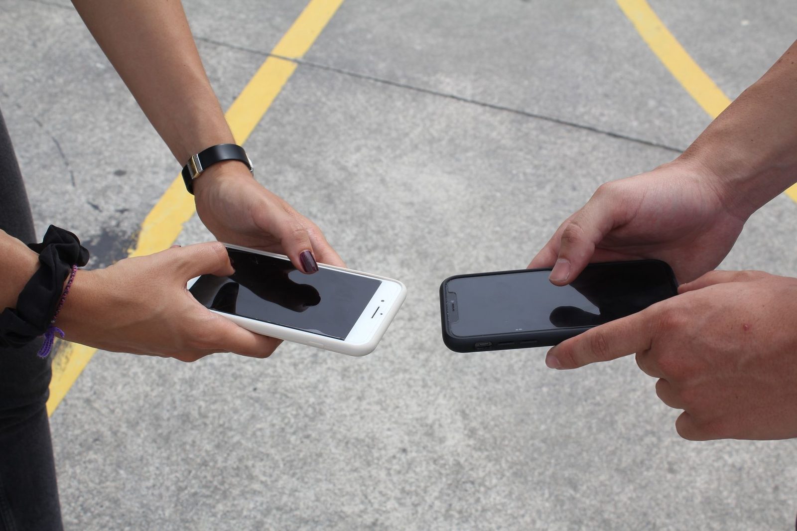 Due persone tengono i loro smartphone uno di fronte all'altro, uno bianco e uno nero, sopra l'asfalto