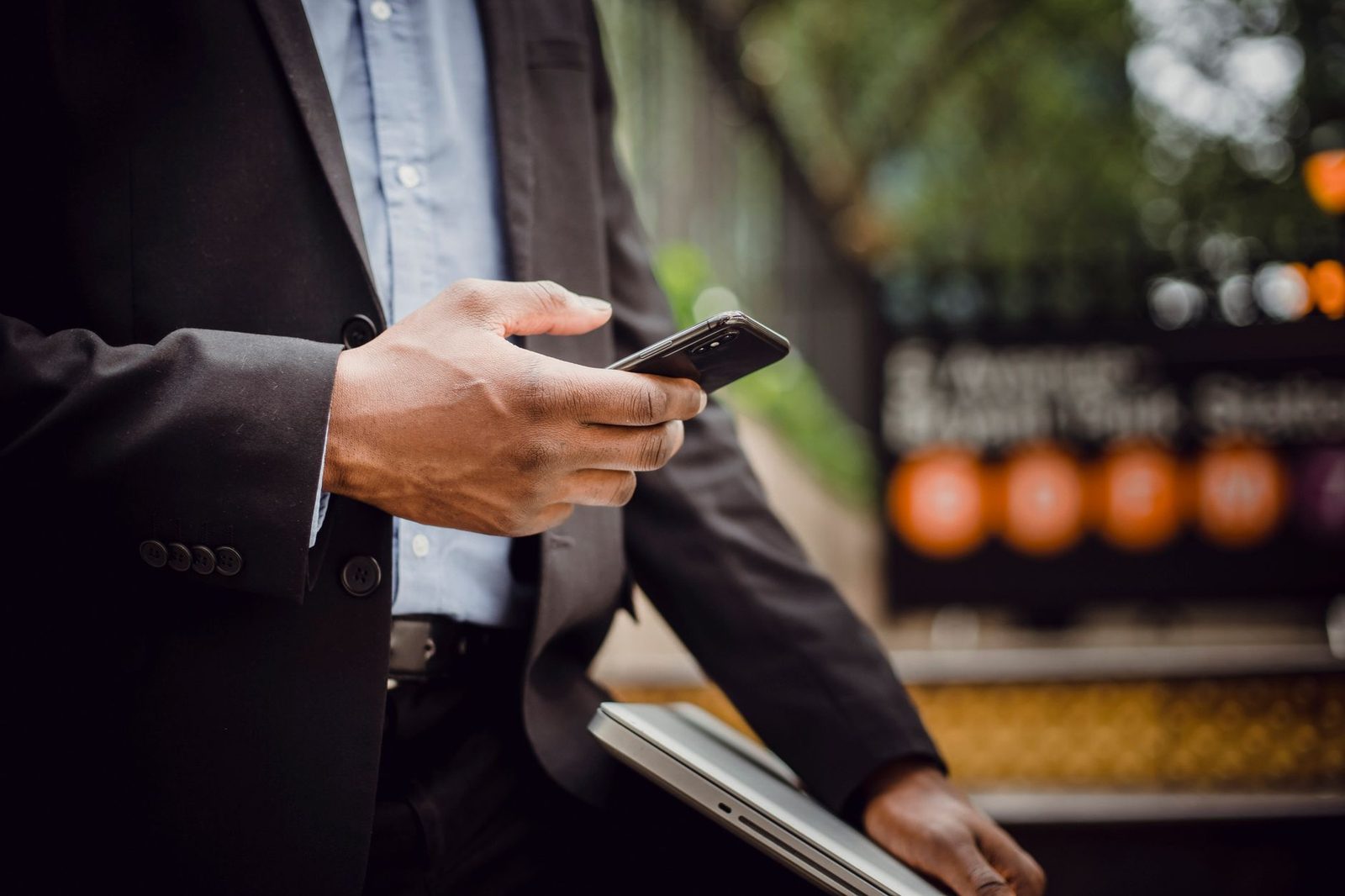 Hombre en traje usando su smartphone en la calle, con un ordenador portátil bajo el brazo
