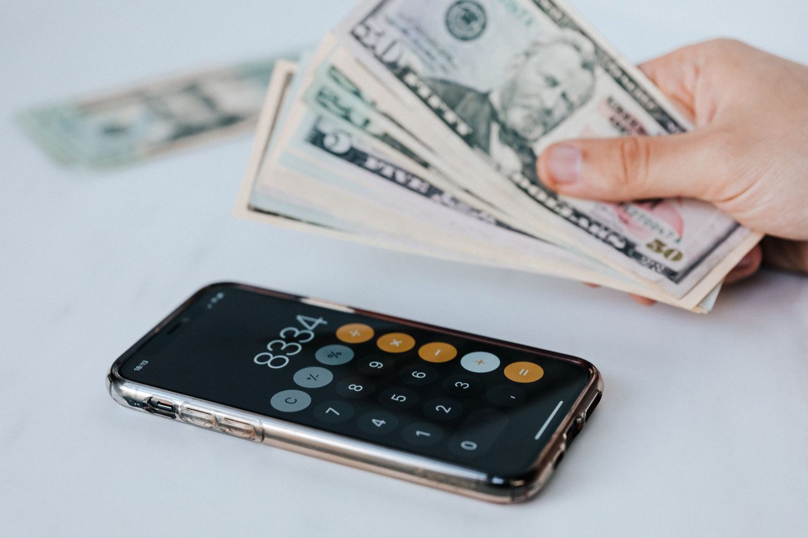 Smartphone affichant une calculatrice posé sur une table et main tenant des billets de banque