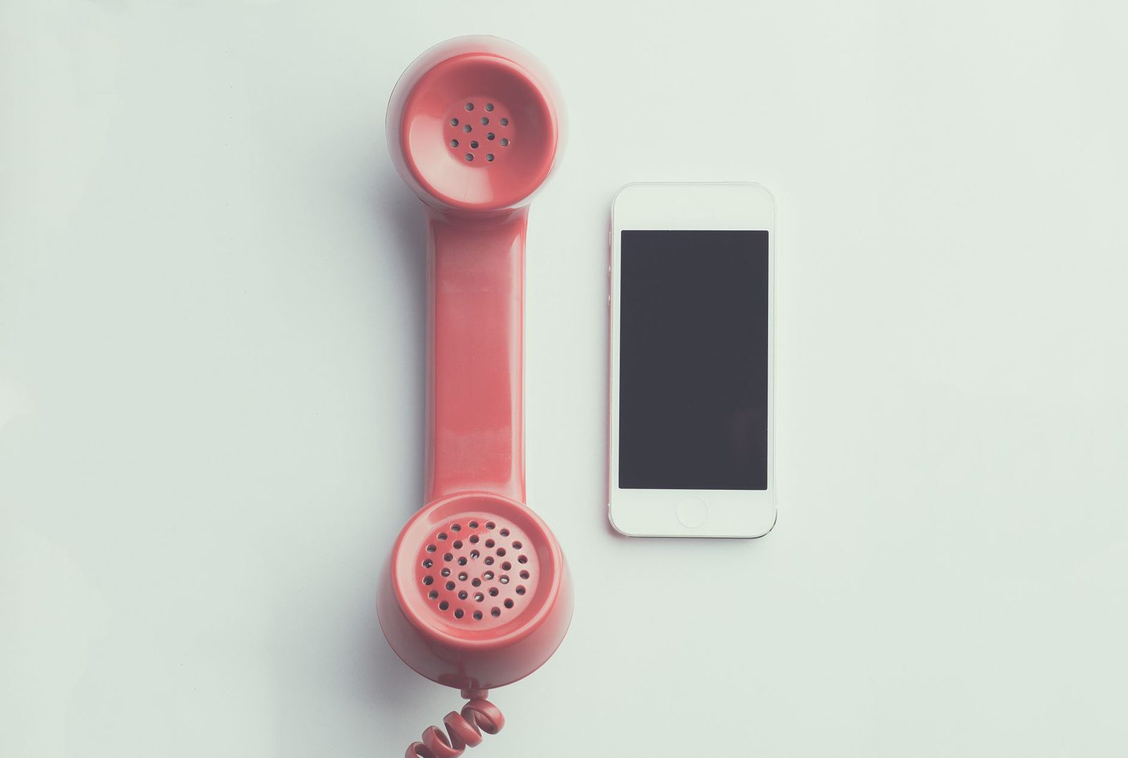 Combiné de téléphone vintage rose posé à côté d'un smartphone blanc sur fond clair