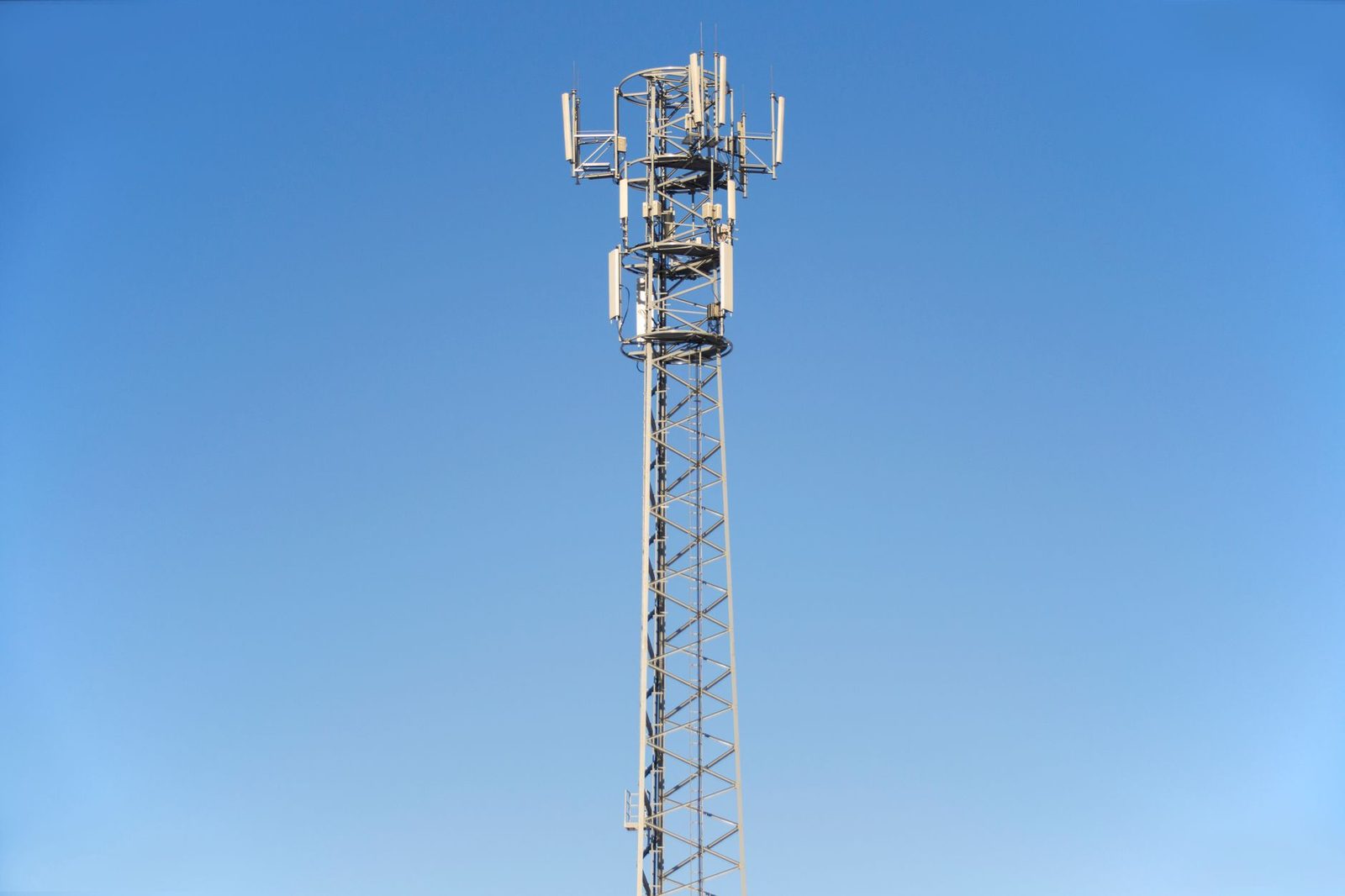 Zendmast voor mobiele telefonie met zenders, afgetekend tegen een onbewolkte blauwe lucht