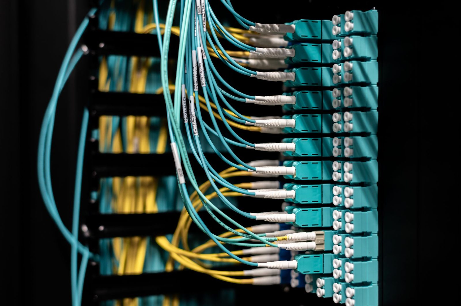 Turquoise en gele glasvezelkabels aangesloten op een patchpaneel in een netwerkrack