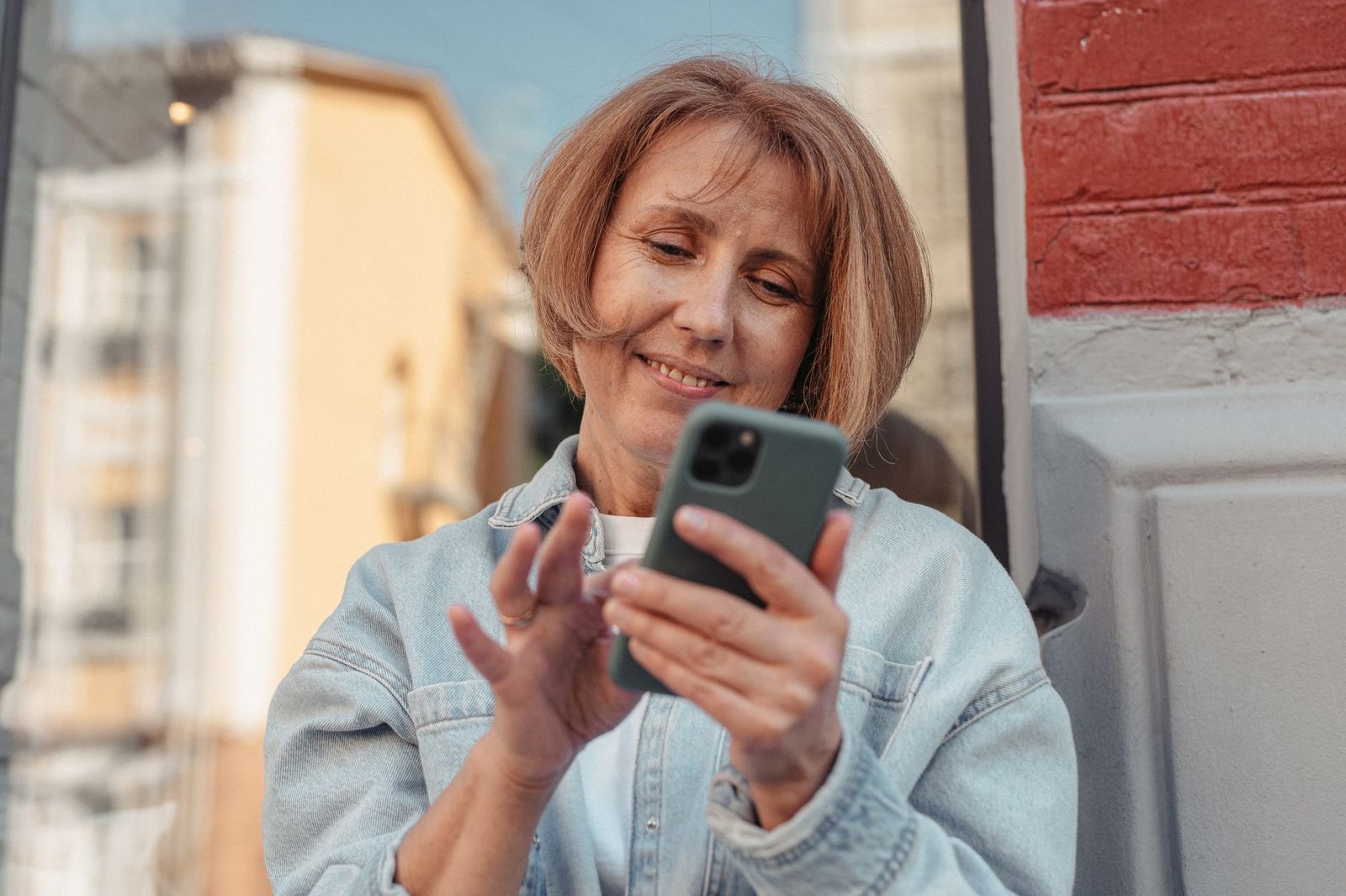 Lachende vrouw in jeansjasje die haar smartphone gebruikt op straat