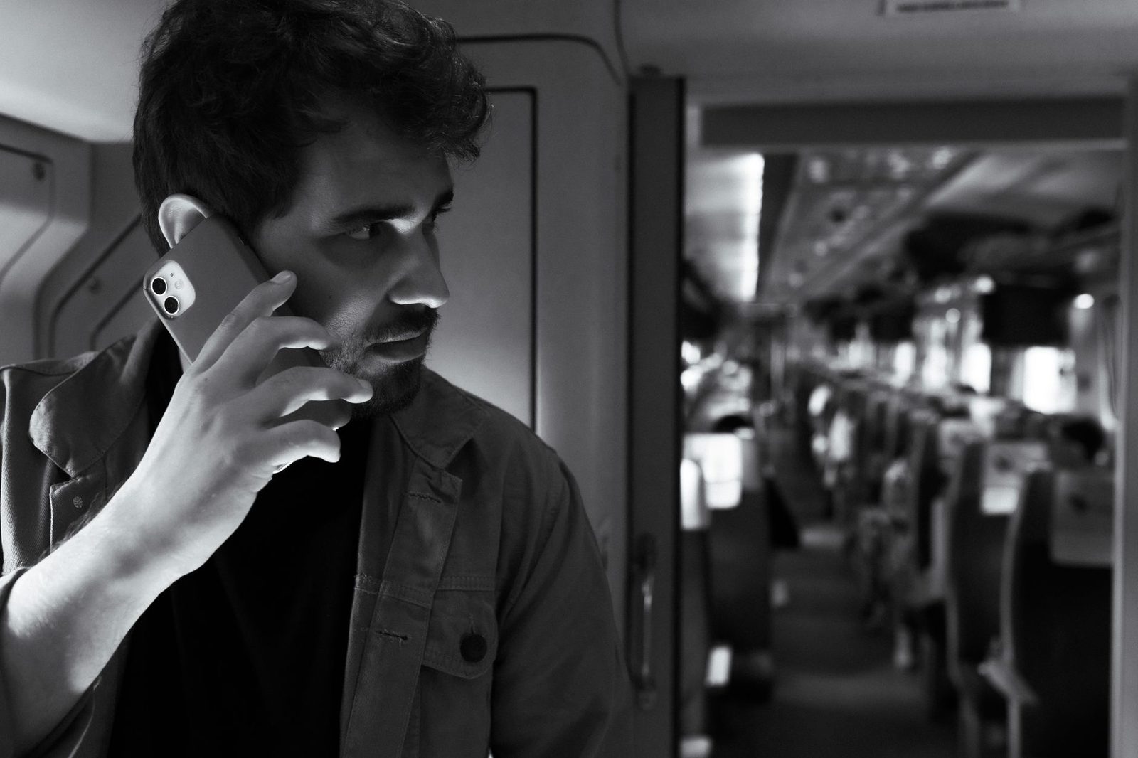 Man holding a smartphone to his ear in a train corridor, black and white photo