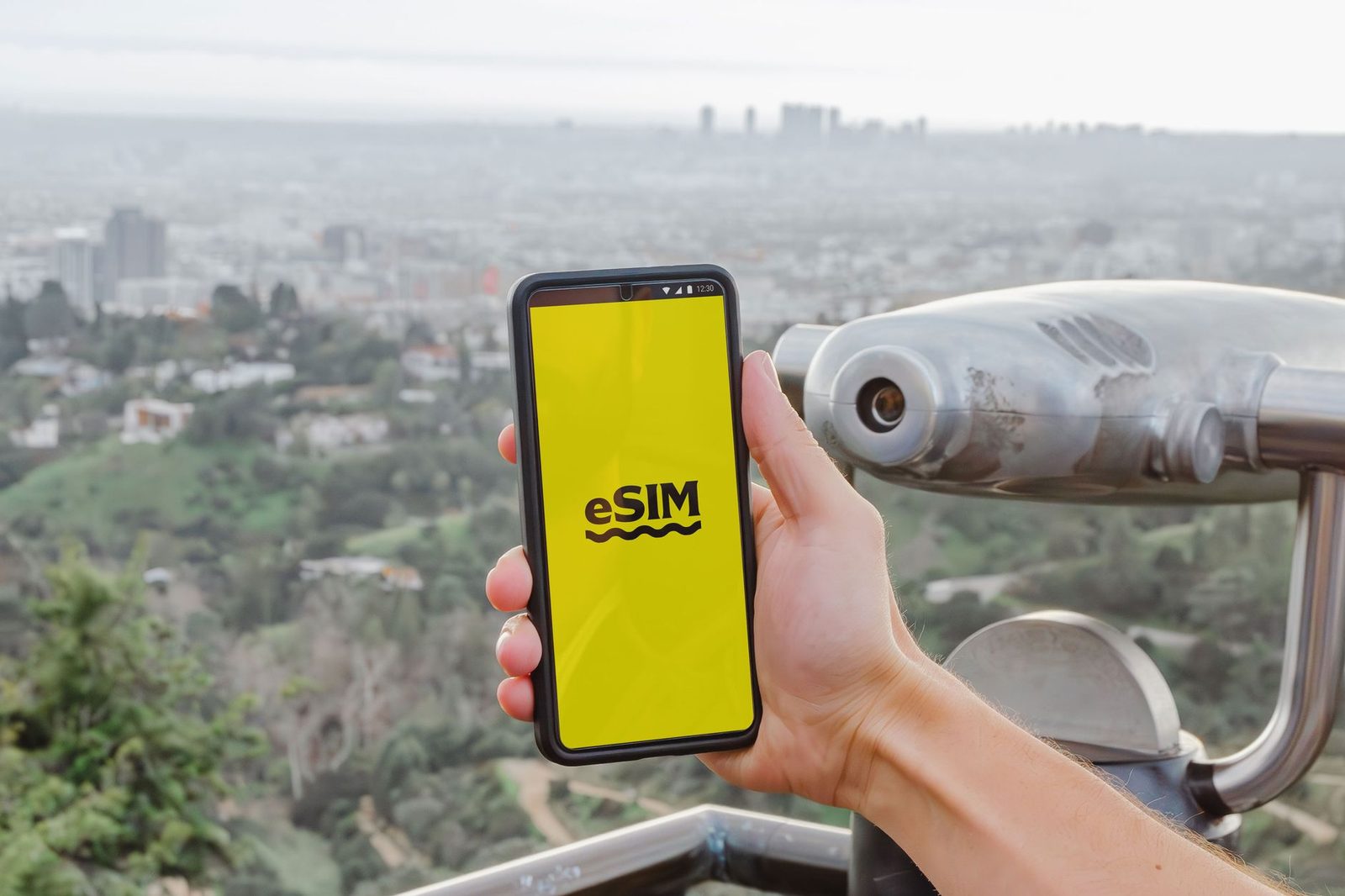 Hand holding a smartphone displaying "eSIM" in front of a city panorama and a viewing telescope