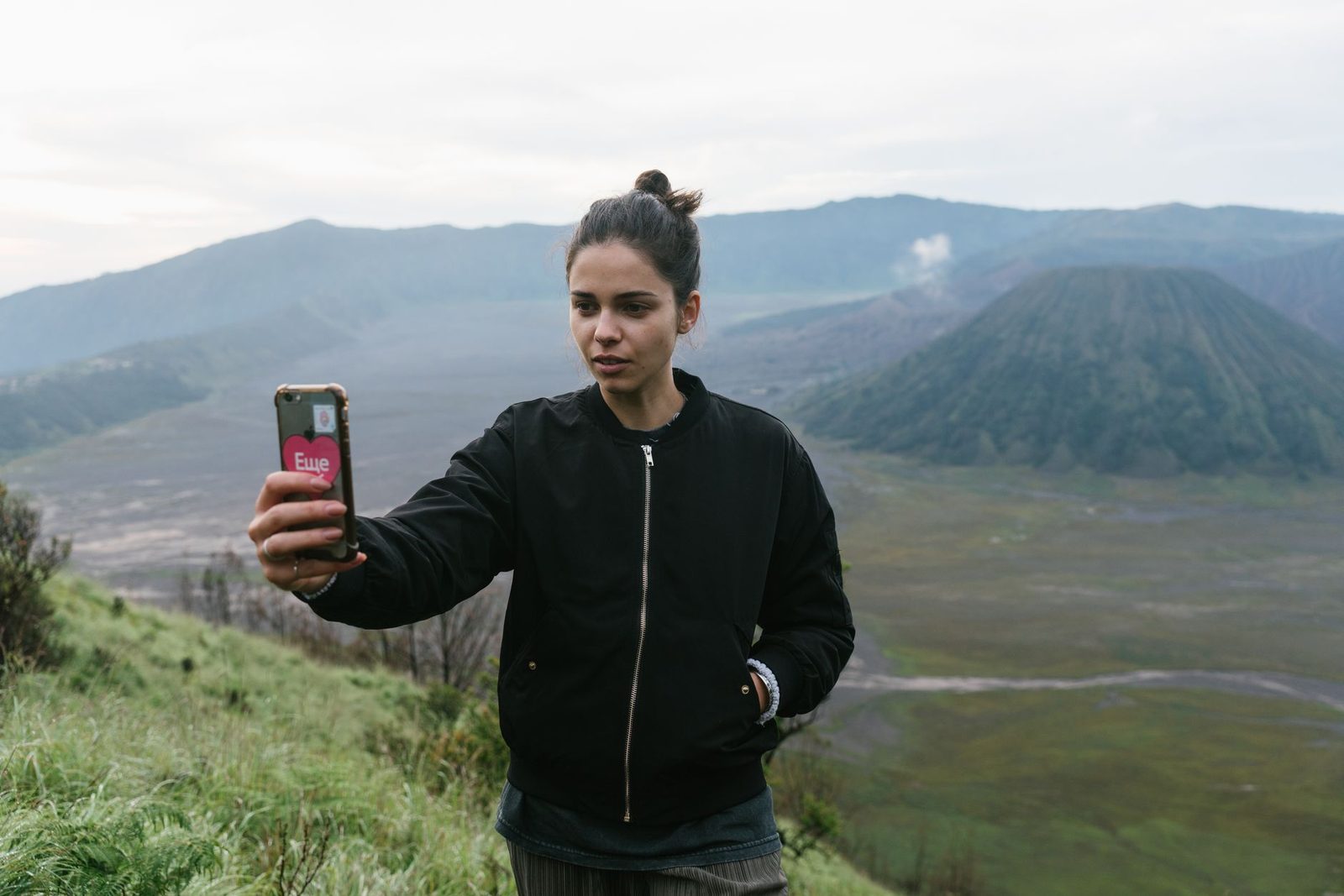 Jeune femme en veste noire utilisant son smartphone devant un paysage de montagnes et de volcan