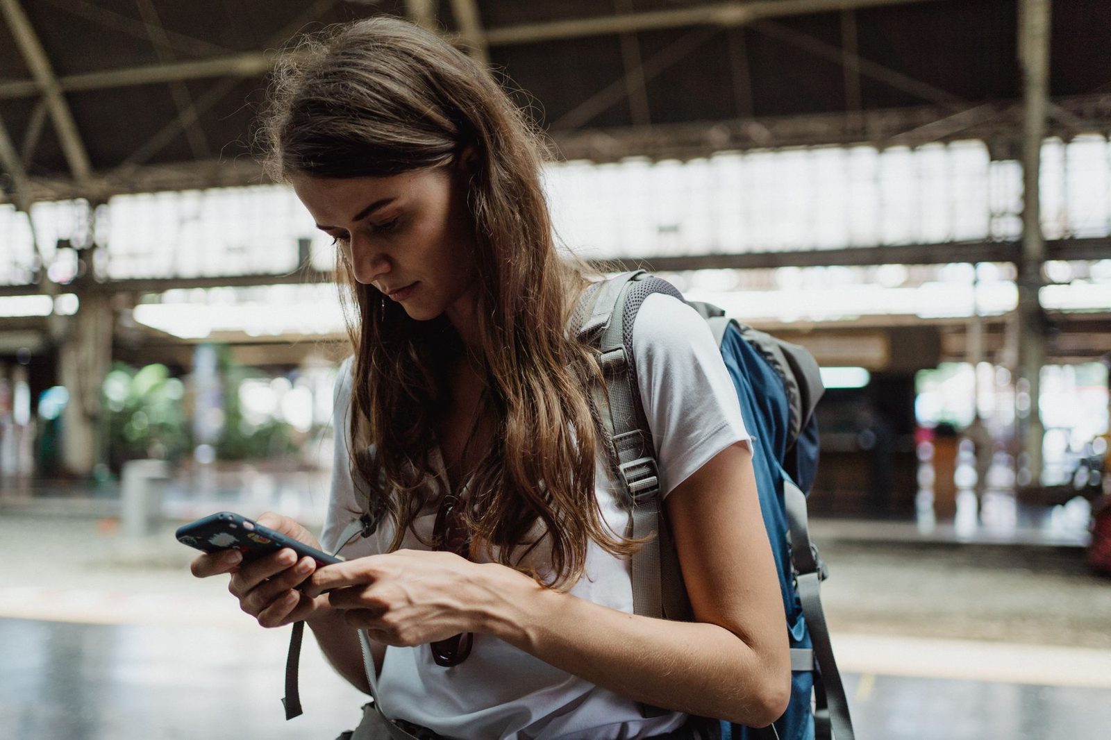 Jeune femme avec un sac à dos consultant son smartphone dans une gare