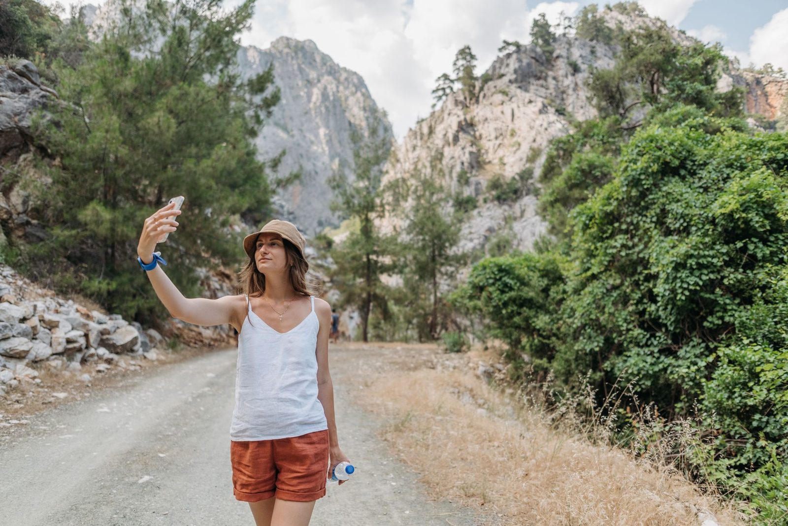 Jeune femme au chapeau prenant un selfie avec son smartphone sur un chemin de montagne