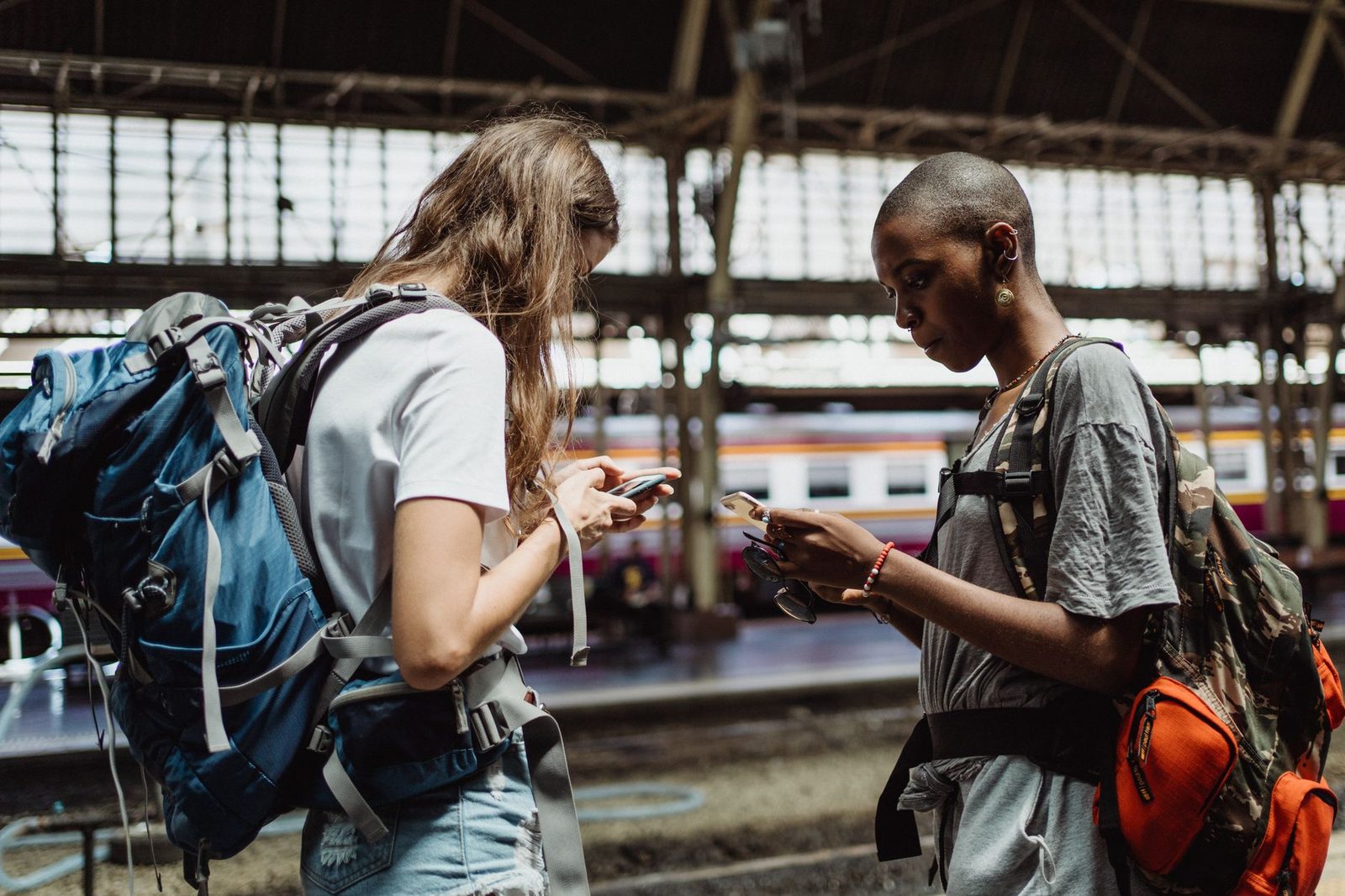 Deux voyageuses avec sacs à dos consultent leur téléphone portable sur un quai de gare