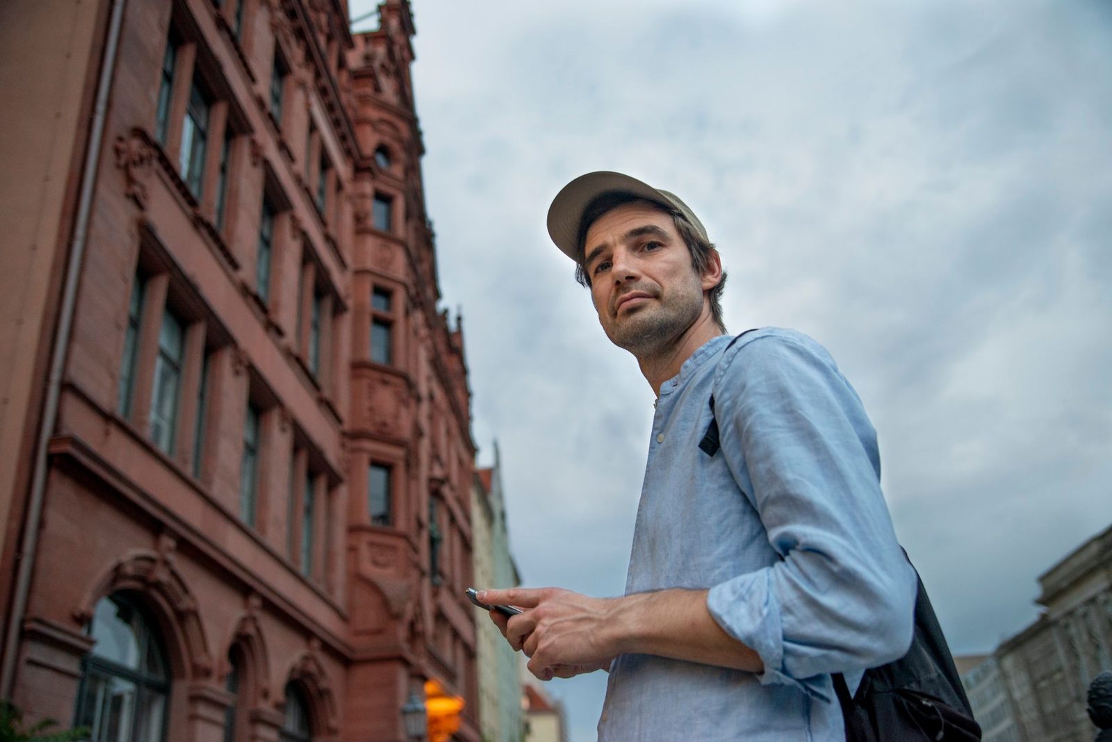 Homme avec casquette et sac à dos consultant son smartphone devant un bâtiment ancien en ville