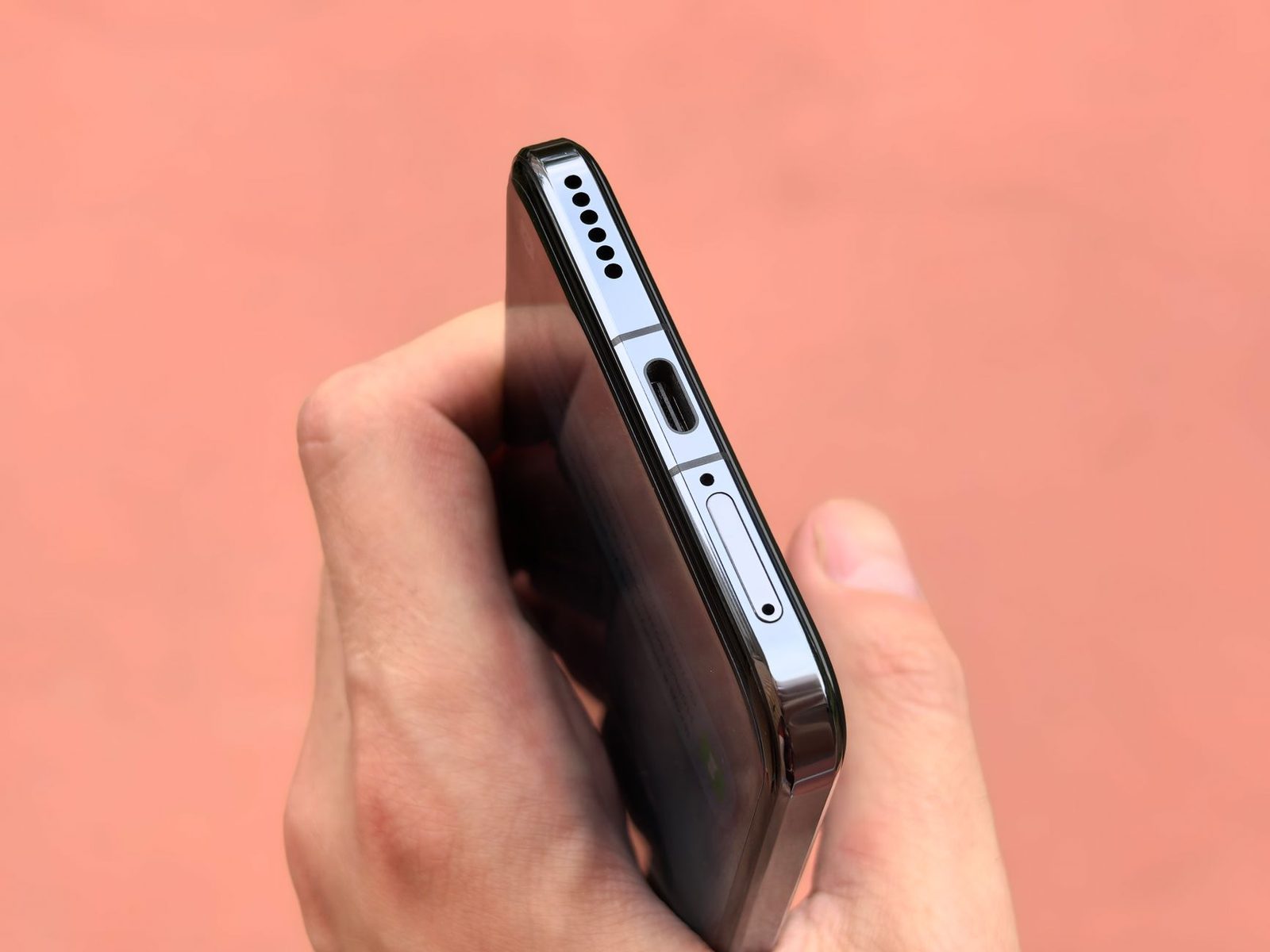 Hand holding a smartphone showing its bottom edge with the USB-C port and SIM card tray